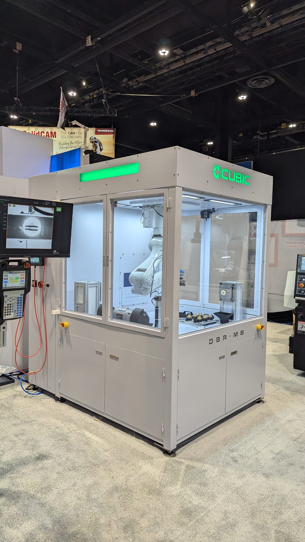 Fully guarded robotic deburring cell with glass panels, green status light bar, external operator monitor and teach pendant