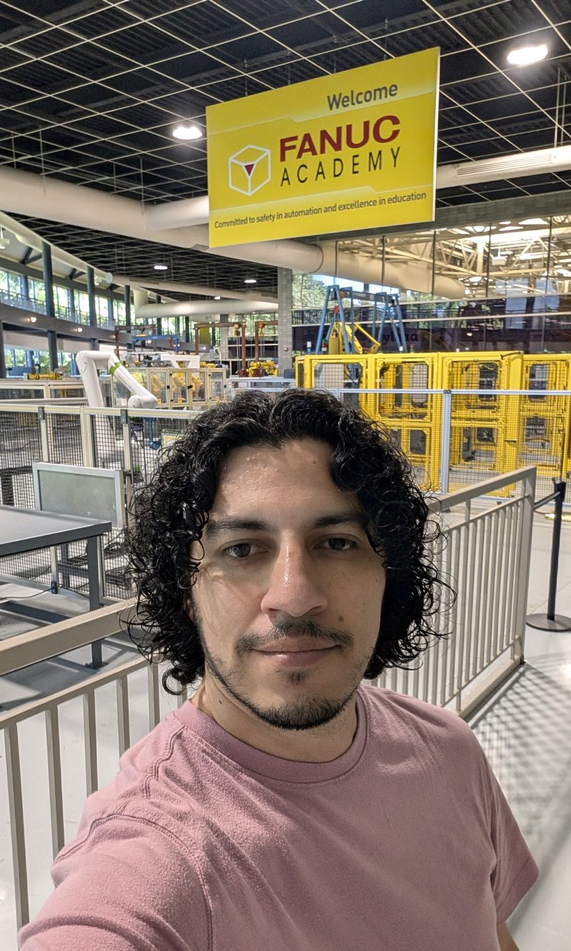 David Facio under a Welcome FANUC Academy banner overlooking the FANUC training floor in Rochester Hills, Michigan