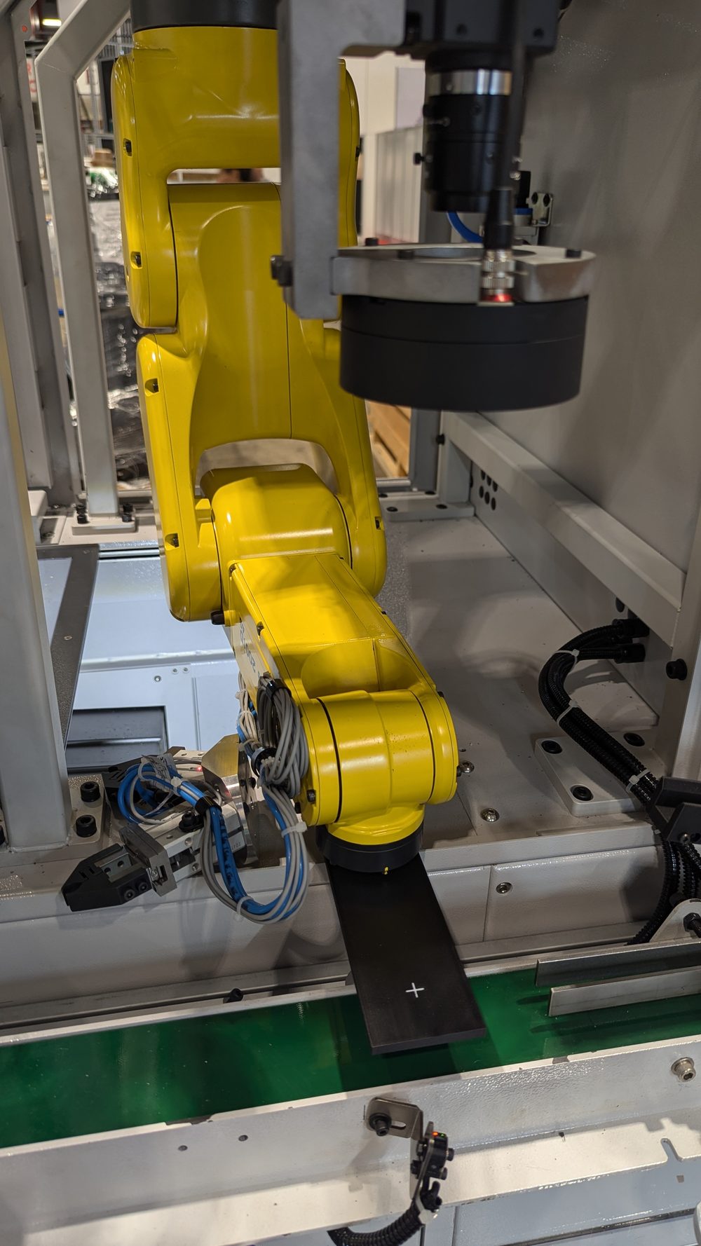 FANUC LR Mate robot arm with dual pneumatic gripper reaching toward an infeed conveyor beneath a fixed overhead machine-vision camera